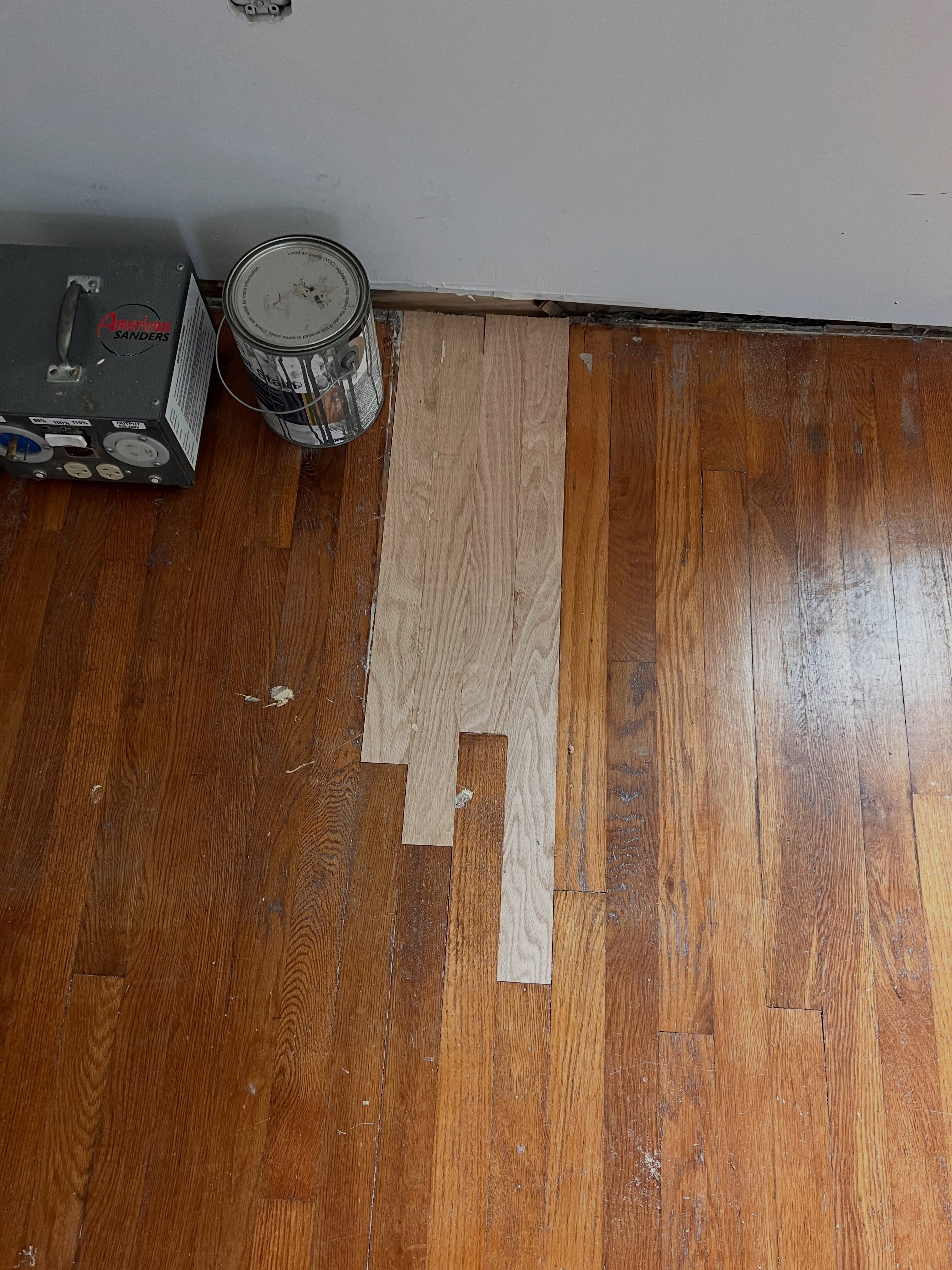 Flooring installation in progress, showing existing dark wood with new light wood planks being laid