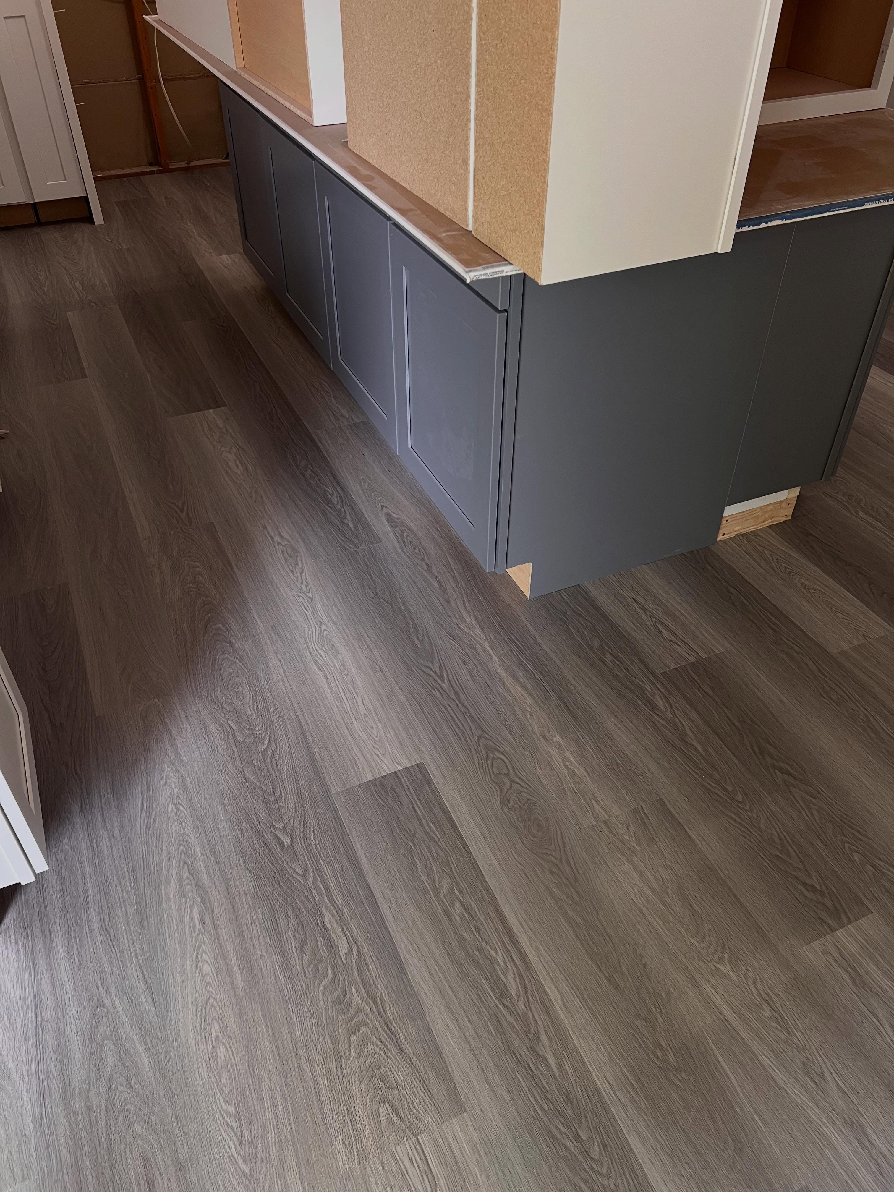 Detail view of luxury vinyl plank flooring alongside a gray wainscot base