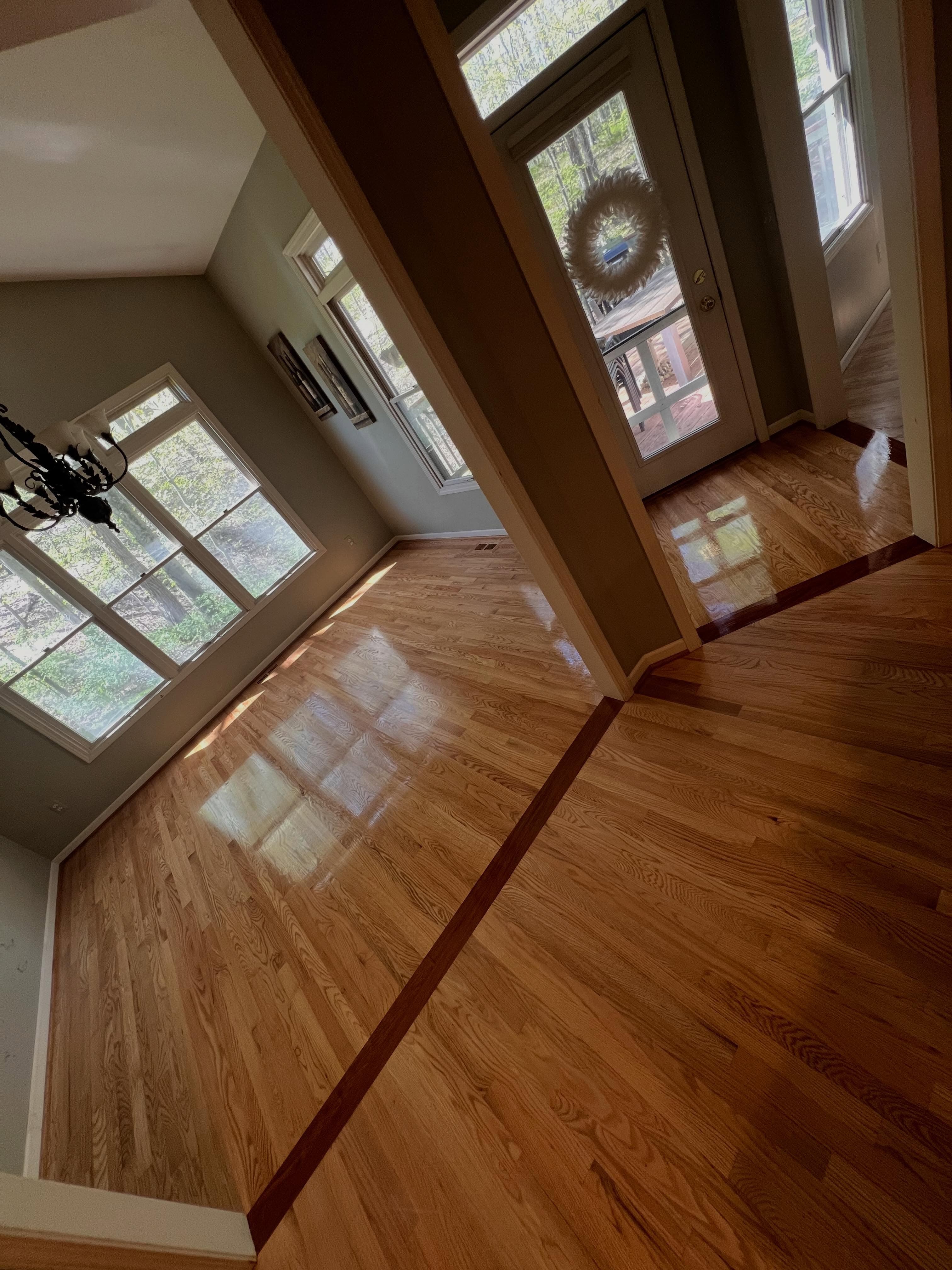 Sunlit entryway with gleaming hardwood flooring in golden-oak tone with two-tone inlay