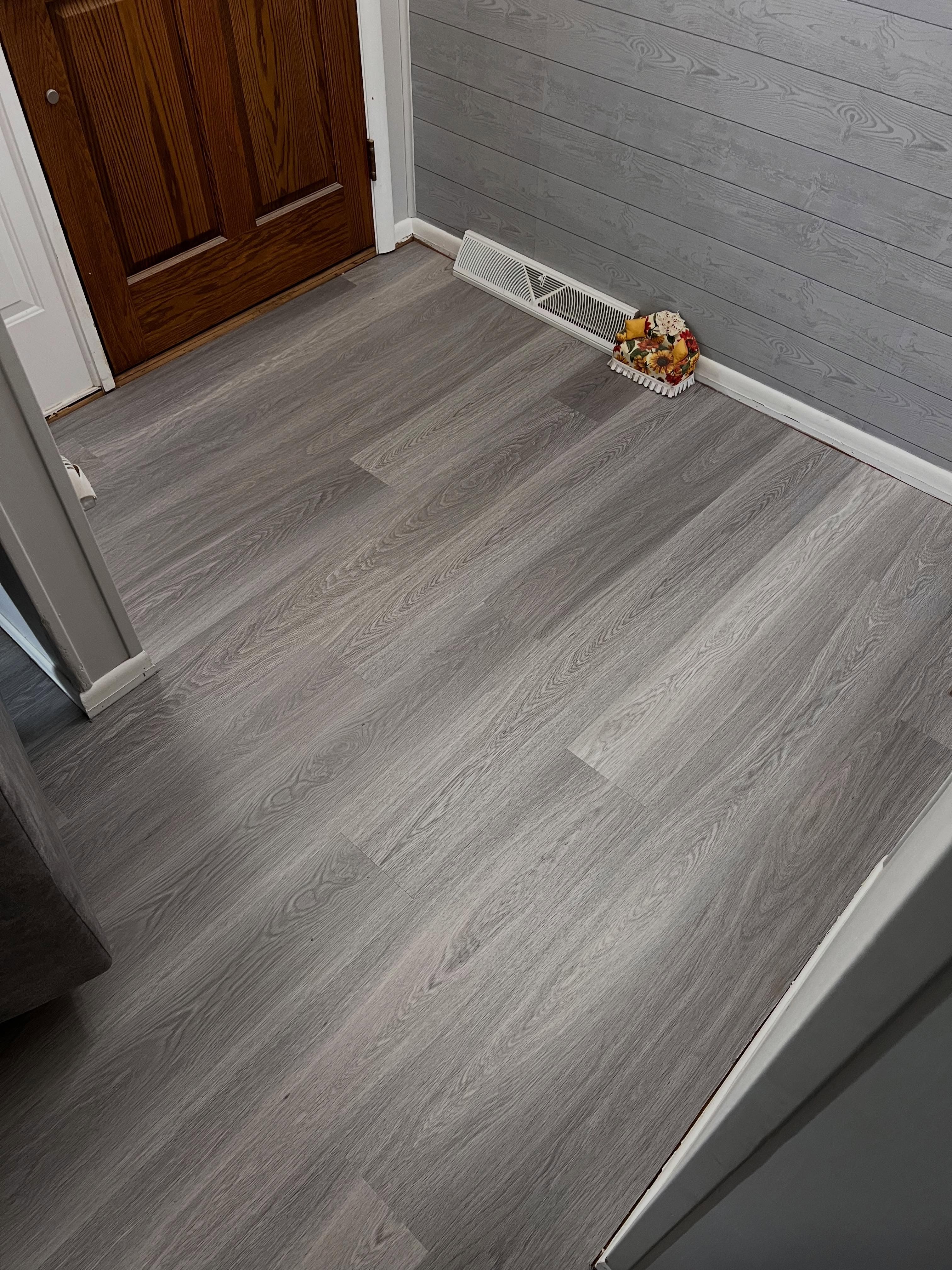 Entryway with gray-tone wood plank flooring, dark wooden door, shiplap wall