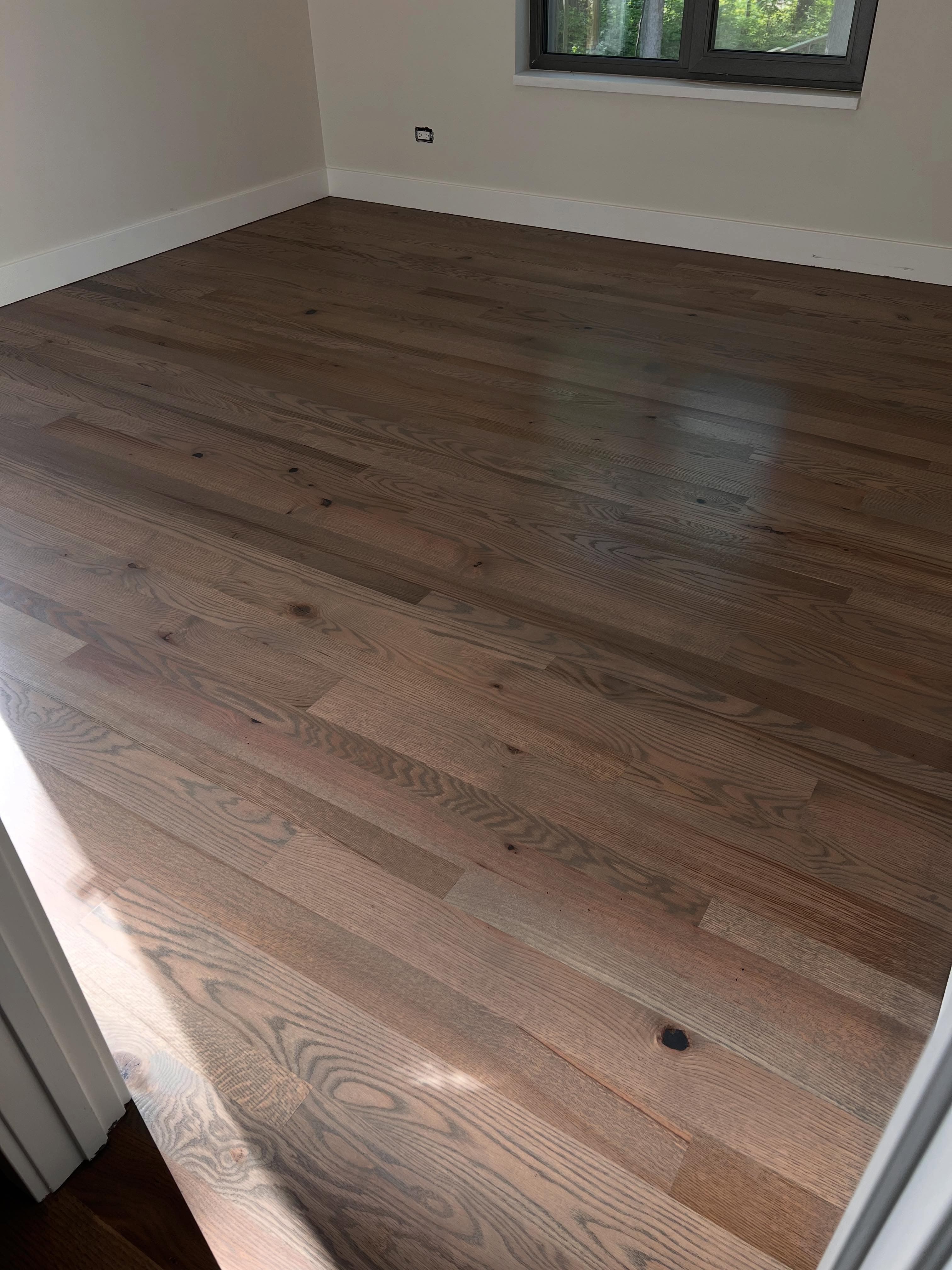 Empty room with newly installed hardwood flooring in medium-brown tone, bright natural light