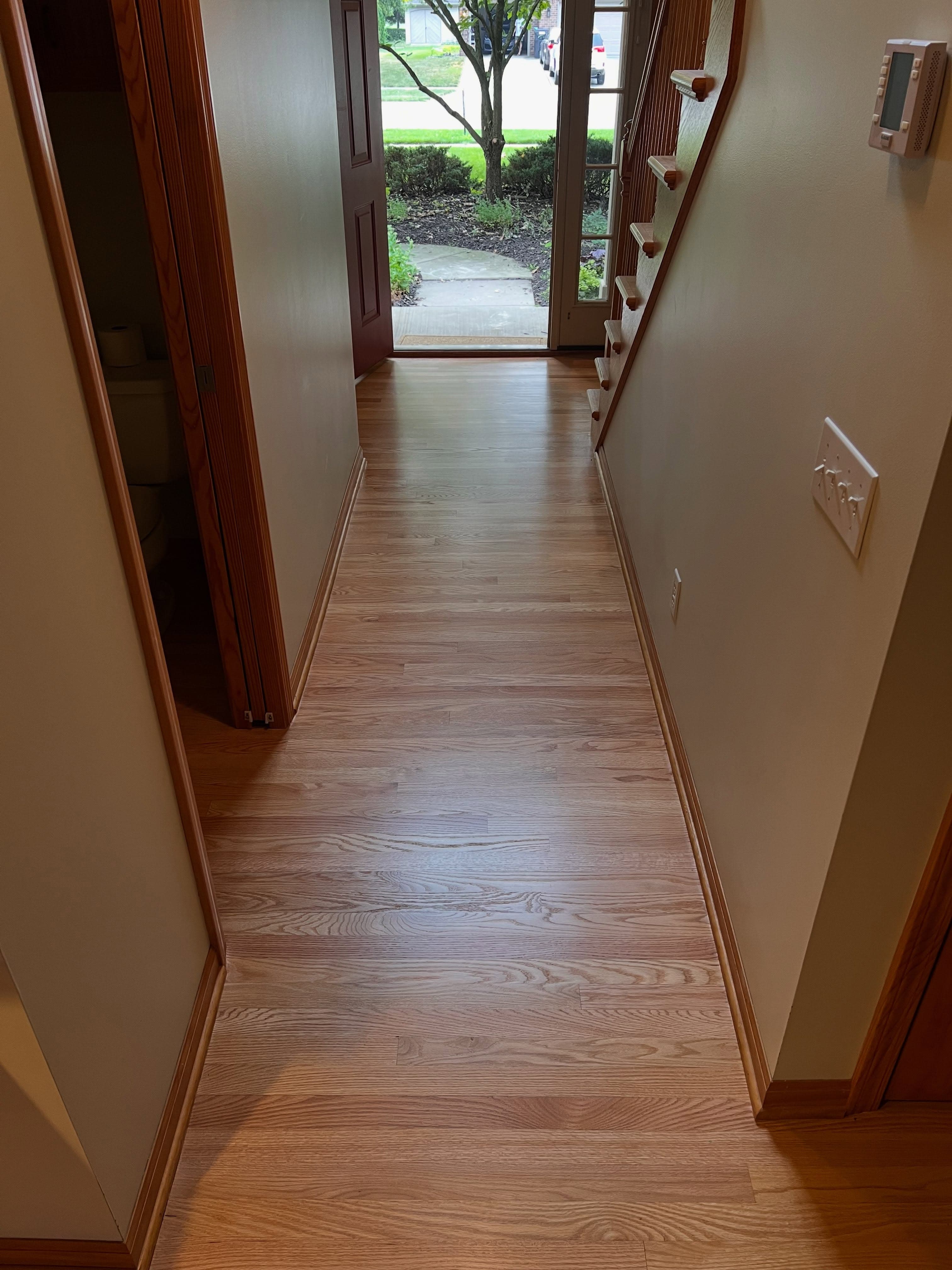 Long hallway with glossy wood plank flooring, decorative baseboards, natural light
