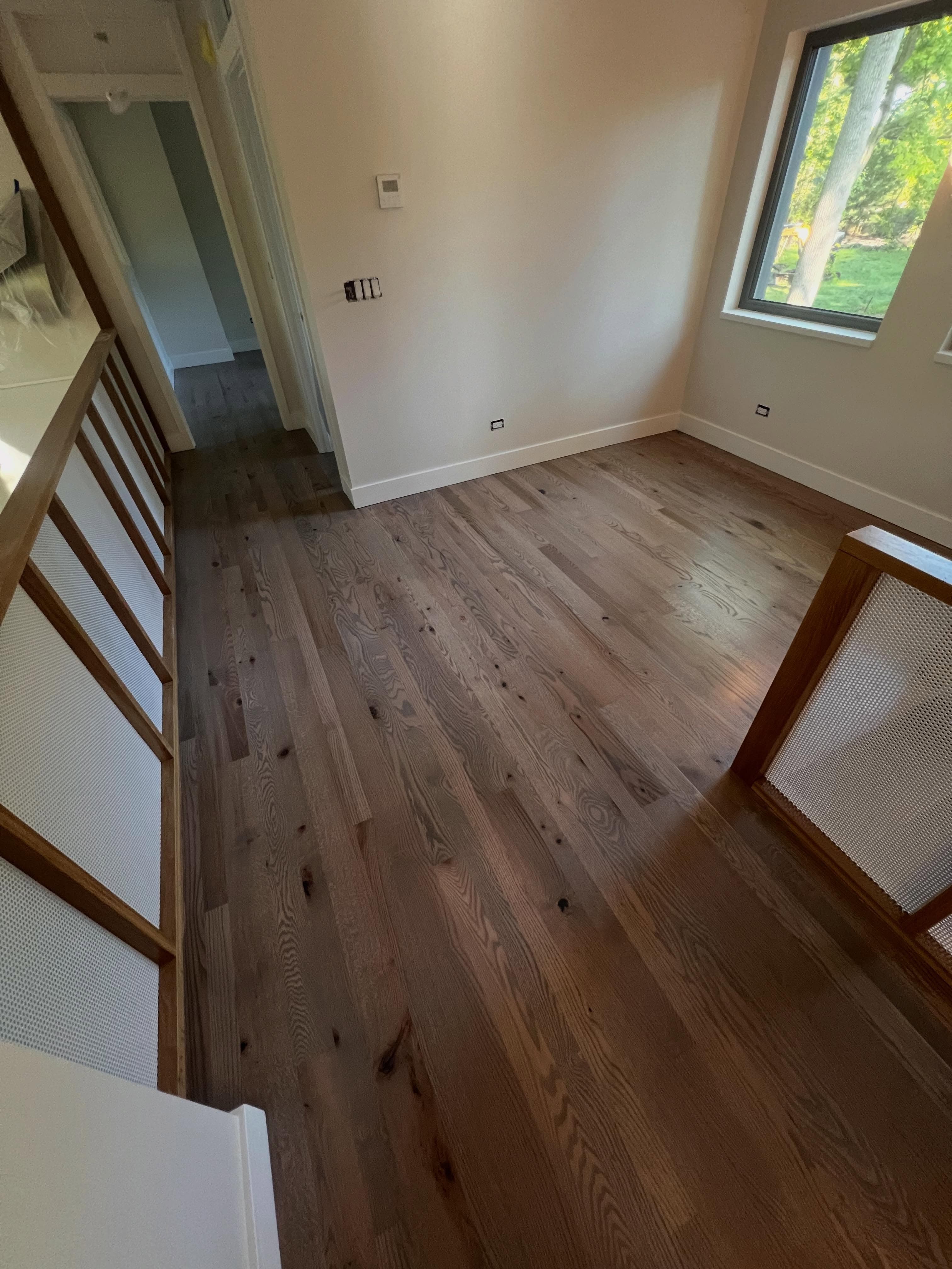 Stairwell with medium-brown hardwood flooring, bright daylight, clean white walls