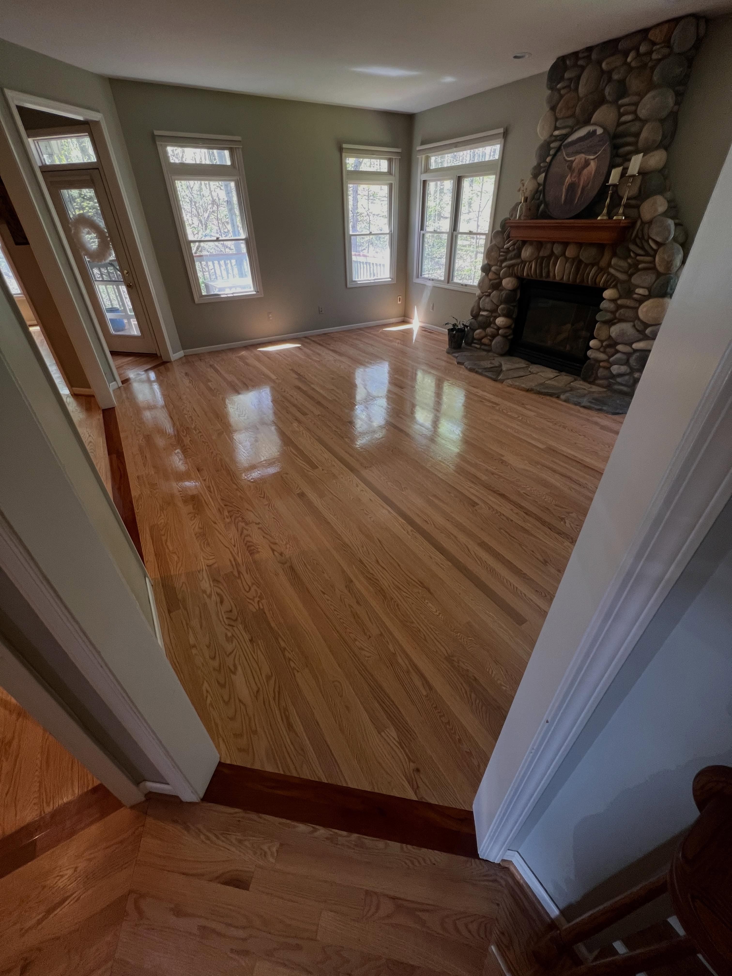 Spacious room with wide-plank hardwood flooring, stone fireplace, large windows with natural light