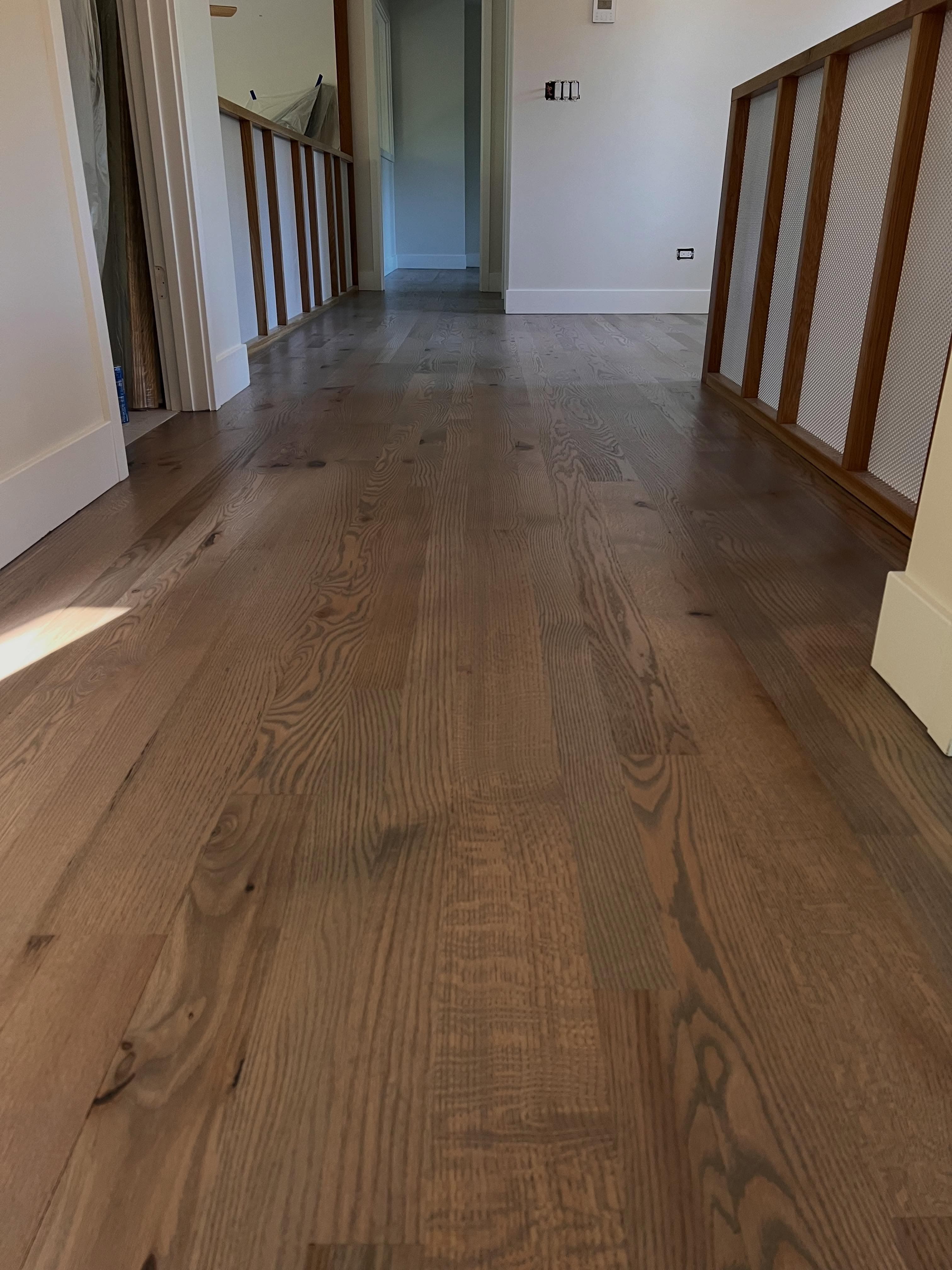 Hallway with newly installed hardwood flooring, staircase visible, white walls